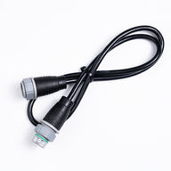 A black jumper cable with two grey and black connectors, one with a green ring, on a white background.