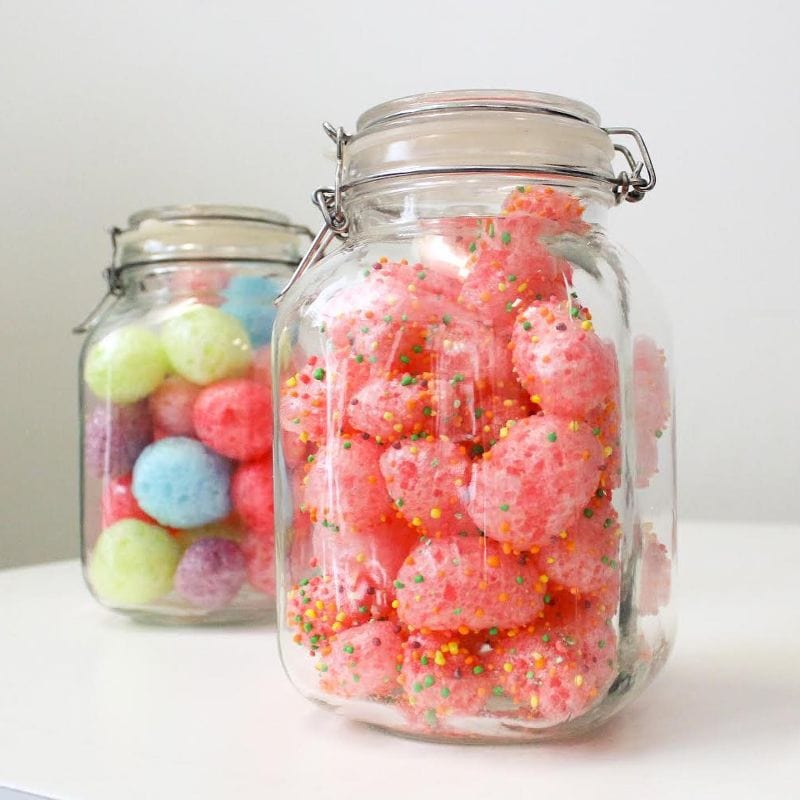 Two glass jars filled with freeze-dried candies. The front jar holds pink sprinkle-covered candies; the back, assorted pastel ones.
