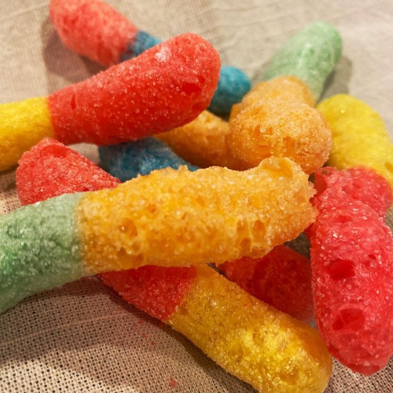 Vibrant pile of red, yellow, orange, green, and blue freeze-dried gummies with a porous, sugary coating.