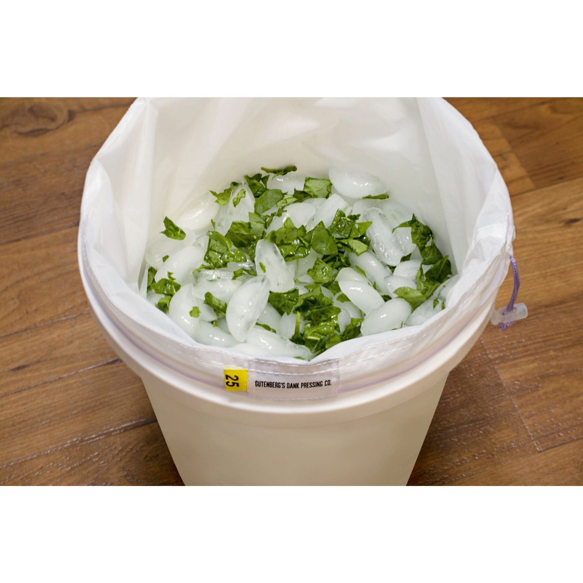 Close-up of a white bucket filled with ice and green chopped herbs, featuring a "GUTENBERG'S DANK PRESSING CO." label and a yellow tag with "25."
