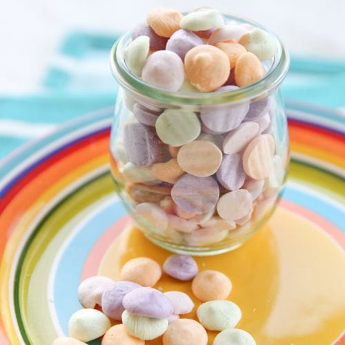 Pastel freeze-dried candies in a glass jar, spilled onto a yellow and rainbow-striped plate.