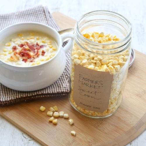 Corn chowder with bacon and a jar of labeled "Farmer's Market" freeze-dried sweet corn on a wooden board.