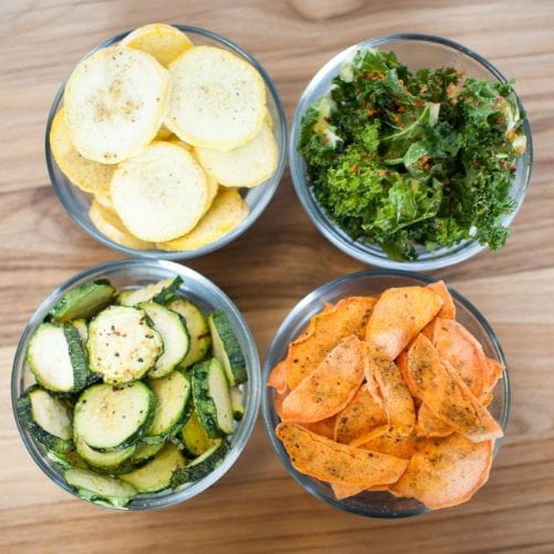 Four bowls of freeze-dried vegetable chips: yellow squash, kale, zucchini, and sweet potato.