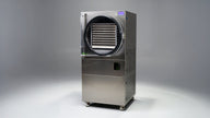 A stainless steel commercial freeze dryer with a glass door showing multiple trays of food.