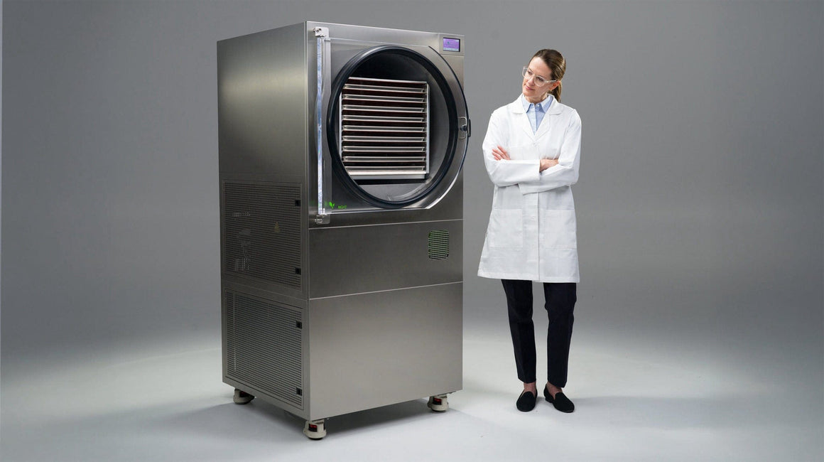 A scientist stands beside a commercial freeze dryer with its door open, revealing trays of food.
