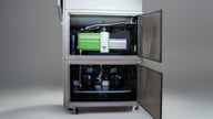 Green vacuum pump and two black compressors inside commercial freeze dryer.