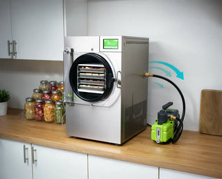 Vacuum pump connected to a stainless steel freeze dryer with food inside, on a kitchen counter.